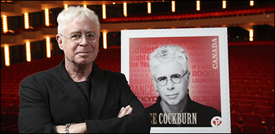 Bruce Cockburn poses with his forthcoming stamp, from True North Records
